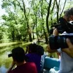 Un grup de patru persoane călătorește cu o barcă mică printr-o zonă împădurită luxuriantă și verde din Sulina. Două au camere profesionale, care surprind imagini ale împrejurimilor senine. Apa este calmă, reflectând frunzișul dens sub lumina strălucitoare a zilei - un cadru ideal pentru excursii lui Nearchus Nautictour în Delta Dunarii.